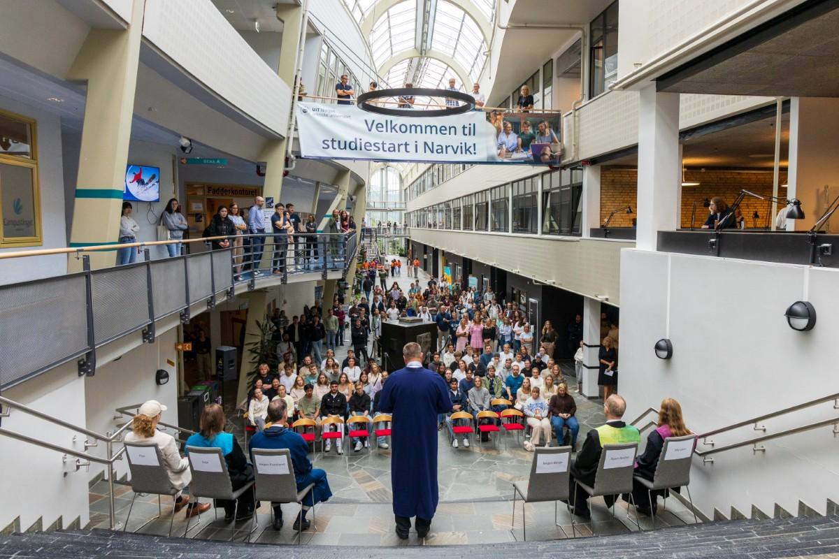 250811 Jørgen Berge ønsker velkommen Studiestart i Narvik foto Vilde Øines Nybakken (8).jpg Mann i kappe holder tale for studenter inne på et staselig universitetsbygg